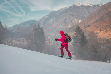 Ski touring woman in pink clothing is slowly ascending on a snowy ski slope, with majestical...