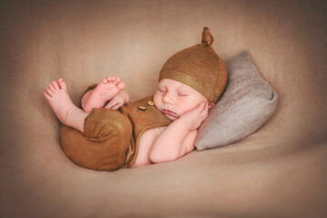 A newborn baby sleeps sweetly on a pillow. Baby in a brown bodysuit and a brown hat. Younger...