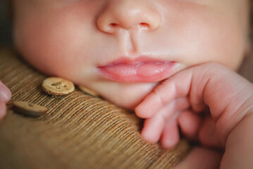 lose-up of a newborn's face. Lips, nose, pen.
A newborn baby sleeps sweetly on a pillow. Baby in a brown bodysuit and a brown hat. Younger brother. Portrait of a newborn. The baby gently touches his  - obrazy, fototapety, plakaty
