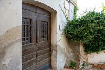 Fototapeta na wymiar Antique wooden door, entrance to the house. Stone walls, green climbing plant. The street of the Italian city. A trip to Europe. Holidays, tourism, sightseeing, beautiful architecture.