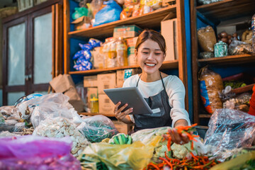 asian female vegetable seller checking supplies using tablet