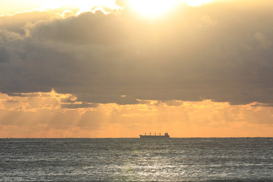 commercial cargo ship sailing in the sun and dark clouds