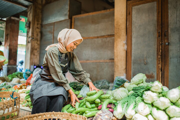 asian hijab greengrocery seller arranging vegetables at her stall