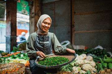female asian seller checking greens at vegetable stall in farmer market