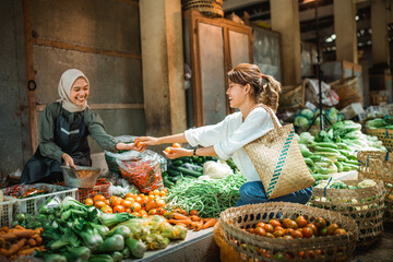 happy grocery seller helping customer choosing greengroceries from grocery stall in farmer market