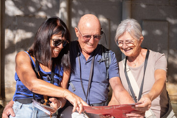 Joyful group of senior friends visiting Granada listening to information via audio guide. Elderly man and two women enjoying vacation and retirement in Europe