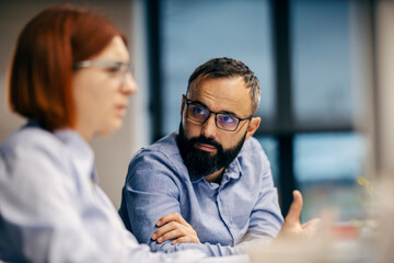 Portrait of a businessman sitting at office and listening to his colleague.