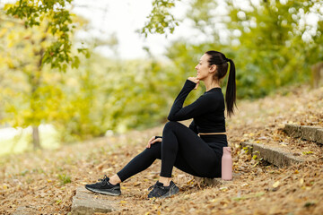 Side view of a sportswoman sitting on stairs in nature and taking a break.