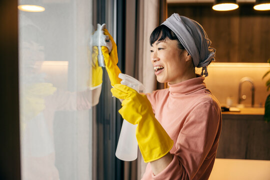 A worthy asian maid cleaning window at home with cloth and detergent.