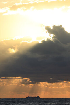 commercial cargo ship sailing in the sun and dark clouds