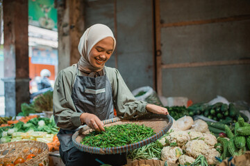 asian female greengrocery seller checking on vegetable products in her stall