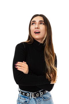 Portrait of beautiful young woman dreaming about something with open mouth, isolated on white background. Adorable twenty year old girl in black turtleneck smiling, looks up and posing in studio.