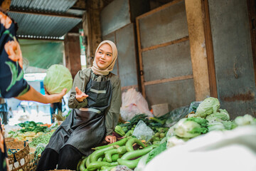 asian hijab vegetable seller helping her customer choosing vegetable