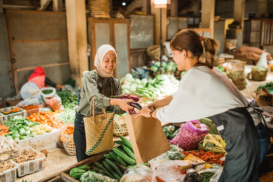 greengrocery seller helping asian customer putting vegetables in paperbag