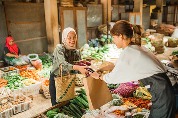 female asian customer getting help from greengrocery seller to putting vegetables in paperbag