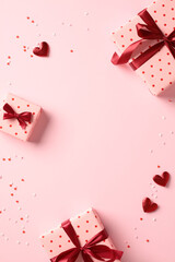 Saint Valentine day holiday vertical background with gift boxes and red hearts on pastel pink background. Flat lay, top view, copy space.