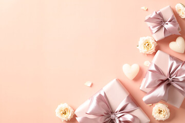 Pastel pink gift boxes with roses and heart shaped candles on beige background. Flat lay, top view.