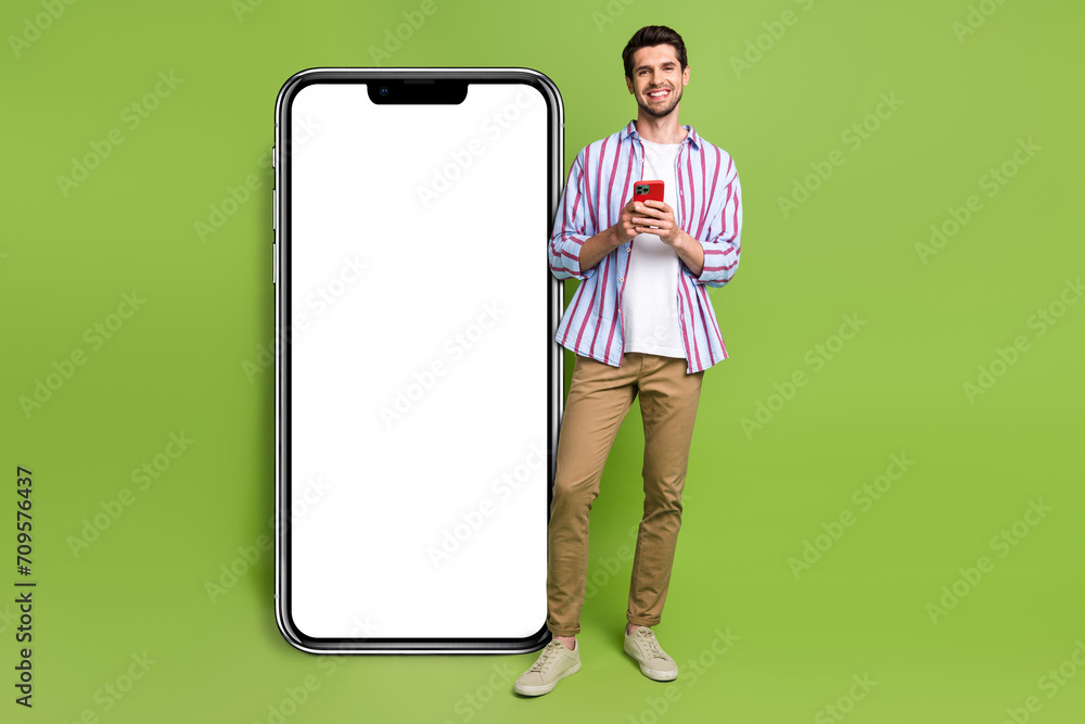 Poster Full size body cadre of young blogger man holding his smartphone browsing scroll tiktok web app display isolated on green color background