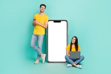 Photo of pretty dreamy married couple wear yellow t-shirts texting looking modern gadget empty...