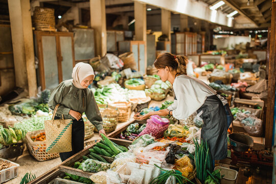 female customer picking vegetable from greengrocery stall in farmer market