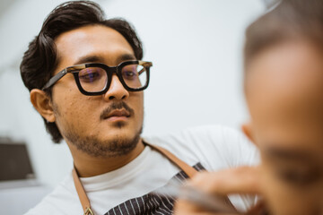 professional asian hairdresser focused on doing his job in barbershop close up view