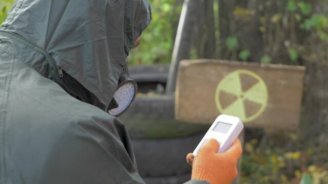 Unrecognized man with radiation mask and geiger counter checks radiation level. Yellow danger sign background in radioactive zone background.