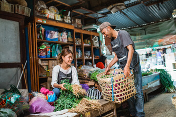 male seller helping his partner to arranging vegetables at farmer market