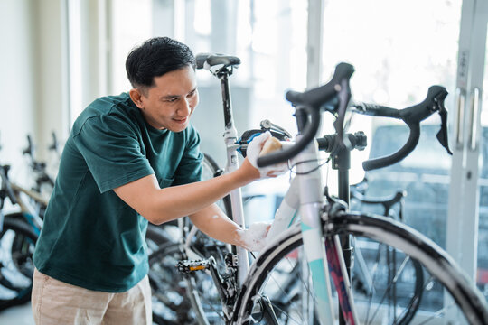 young man smiling while washing a racing bike with foaming soap with a bike shop background