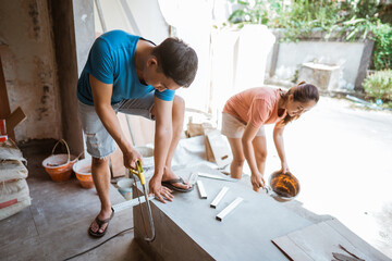 portrait of a husband sawing wood and wife making cement mixture while building a house