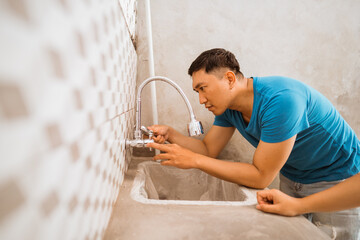 Asian young husband installs dishwasher faucet while building new house