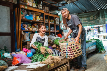 male seller lifting basket and helping his partner to arrange vegetables
