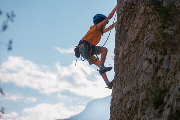 A determined and strong boy climber climbs a steep mountain wall. Extreme sports and rock climbing.