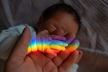 A man holds his newborn son's hand. Beam of light through a prism. 
