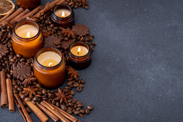 Obraz na płótnie Canvas Soy scented candle in a jar. Coffee beans, anise, cinnamon spices. The candles are burning. Dark copy space background