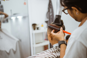 asian male hairdresser drying his customer hair using detangler and hairdryer