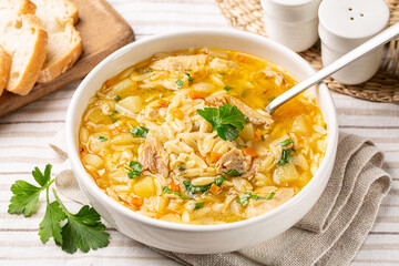 Homemade chicken orzo soup in a white plate, fresh bread. - obrazy, fototapety, plakaty