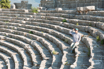 Tourist woman sitting on the steps of The ancient Greek amphitheater at the ancient City