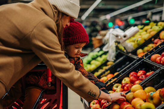 Young woman and son buying apples at supermarket