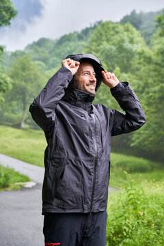 Happy man wearing black jacket and standing in front of trees