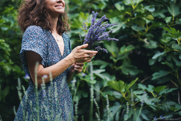 Young cheerful smiling woman standing in a summer garden with a bouquet of lavender in her hands
