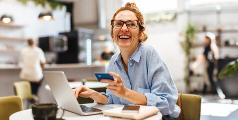 Happy woman enjoying online shopping with her credit card in a restaurant - obrazy, fototapety, plakaty