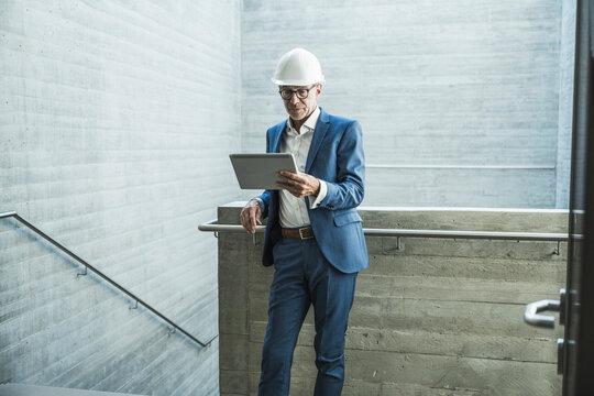 Senior engineer wearing hardhat and using tablet PC near wall