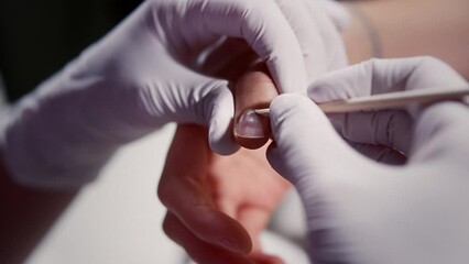 Master in gloves removes cuticle from client nail with wooden pusher in beauty salon closeup. Manicurist takes care of woman fingernails at procedure. Beautician works with customer hands in cabinet