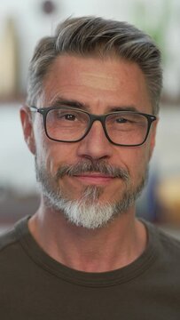 Portrait of happy, confident older man at home looking at camera smiling. Mature age, middle age, mid adult casual guy in 50s, bearded, gray hair, wearing glasses.