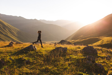 Woman jumping on rocks in front of mountains at sunset