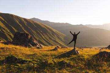 Carefree woman with arms raised standing on rock in front of mountains at sunset