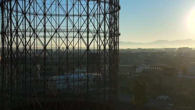Alba sul Gazometro del quartiere post industriale Ostiense a Roma, Italia.
Veduta aerea con drone dei raggi del sole che passano attraverso la vecchia struttura del Gasometro.
