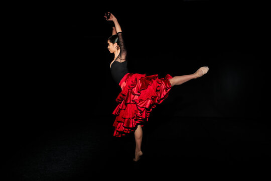 Flamenco student dancing with arms raised against black background