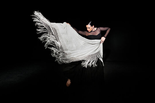 Young flamenco dancer performing with shawl against black background