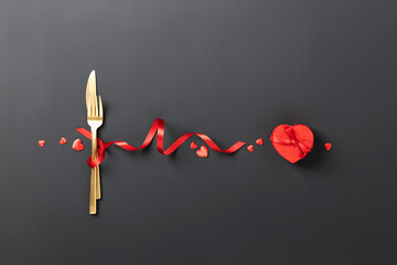 Fork and knife tied with a red ribbon on black background. Romantic dinner. Valentine's Day